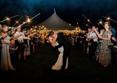 Bride and groom kissing surrounded by wedding party outdoors at night