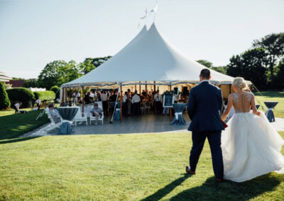 Bride and groom walking towards wedding party underneath outdoor tent