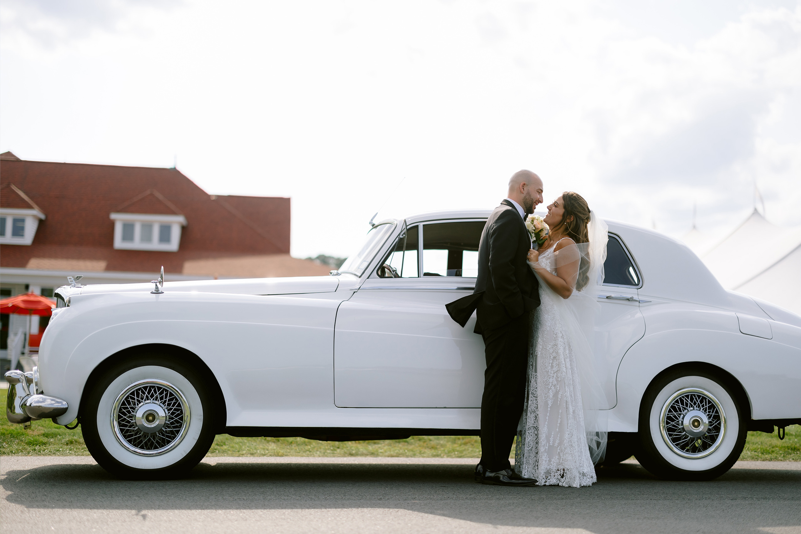 Groom and bride posing next to old fashion white car