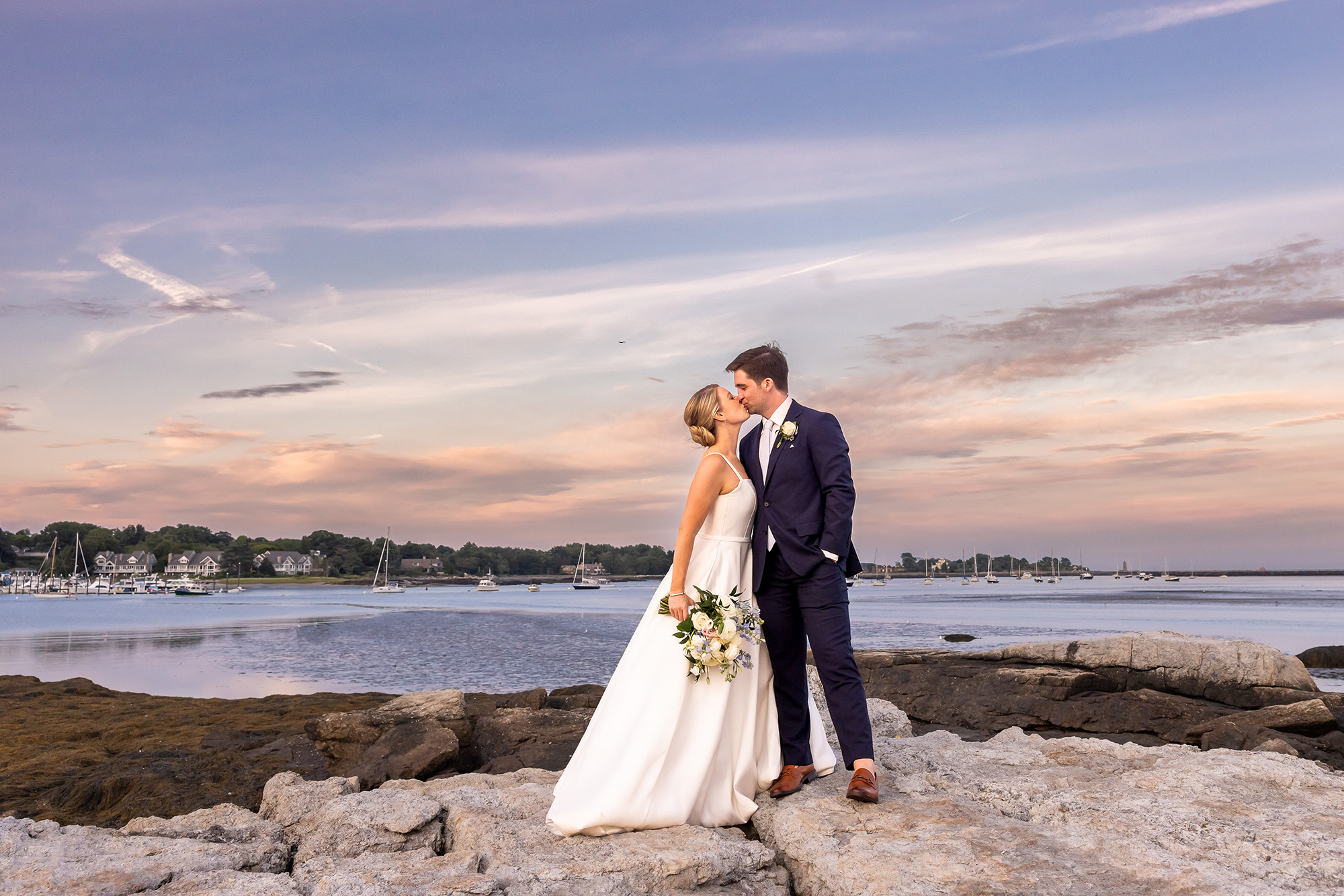 Couple on their wedding day kissing with a scenic ocean shot behind them