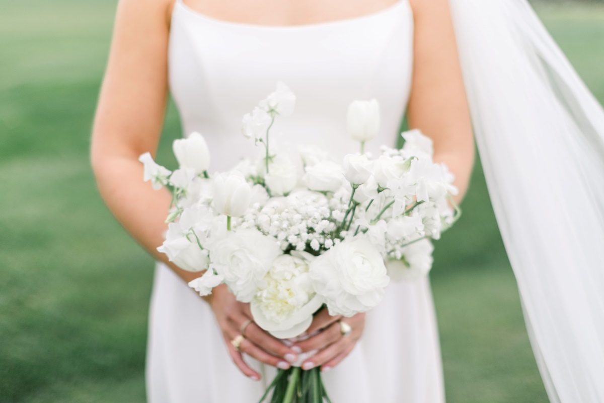 A bride elegantly holds a bouquet of white flowers, symbolizing purity and new beginnings on her special day.