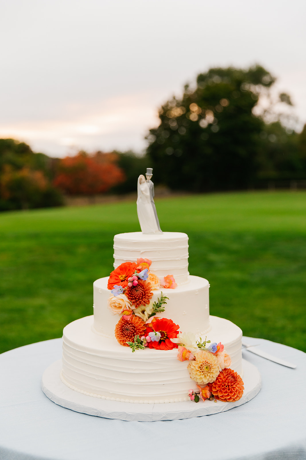 A wedding cake adorned with vibrant orange and red flowers, elegantly placed on top, showcasing a festive desin.<br />
