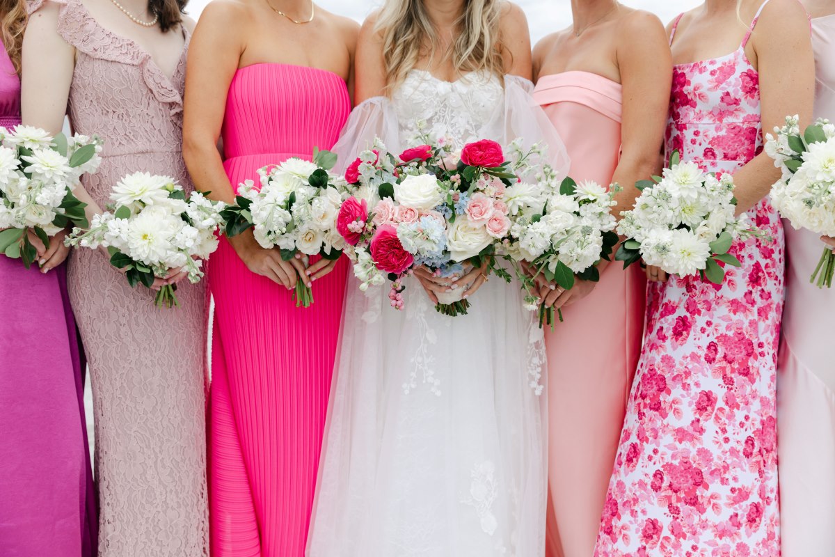  A group of bridesmaids in pink and white dresses, each holding a bouquet, standing together in a joyful celebration.