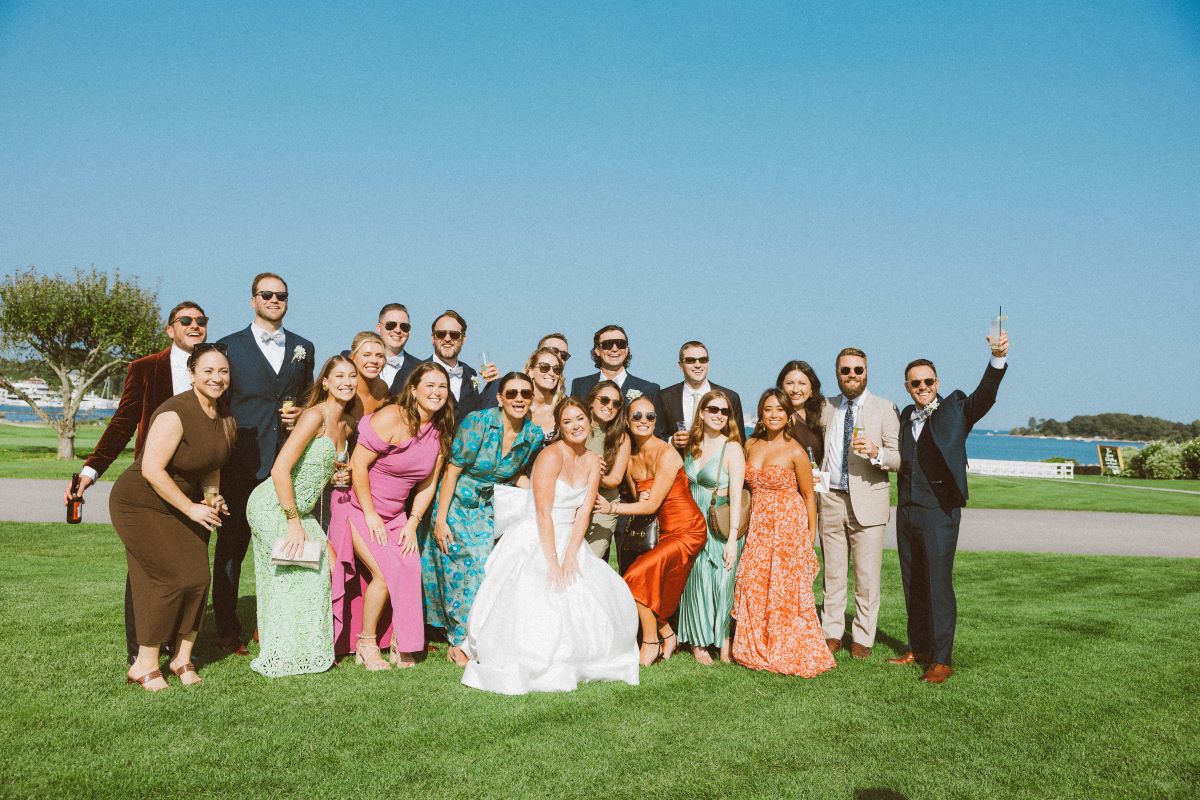  A group of elegantly dressed individuals posing on the grass, celebrating a luxury wedding with smiles and joy.