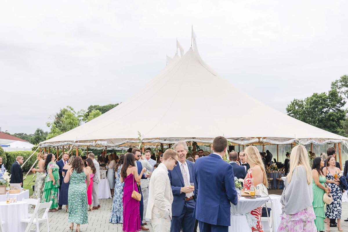 A group of elegantly dressed guests gathered around a luxurious wedding tent, celebrating a special occasion.