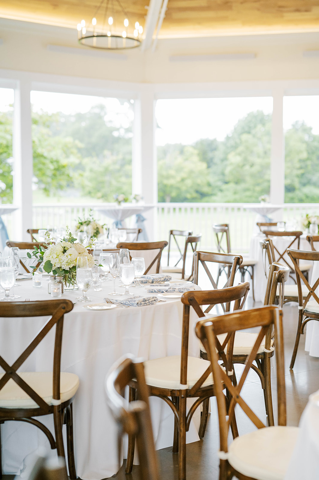 A beautifully arranged wedding reception featuring white tablecloths and elegant wooden chairs, creating a charming atmosphere.