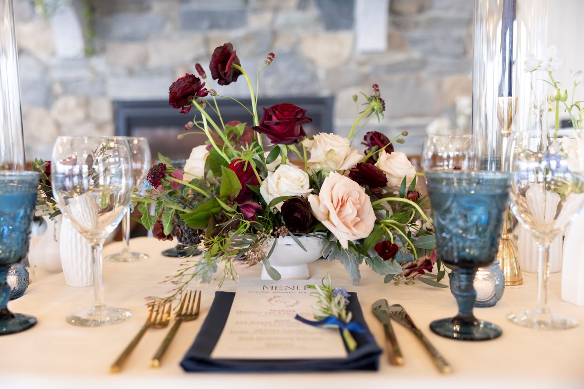 Elegant table setting featuring a white tablecloth adorned with blue and burgundy flowers, perfect for a luxurious wedding.