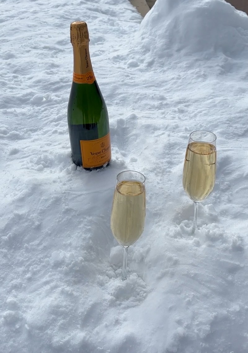 Two elegant champagne flutes in the snow beside a bottle, symbolizing a luxurious wedding celebration.