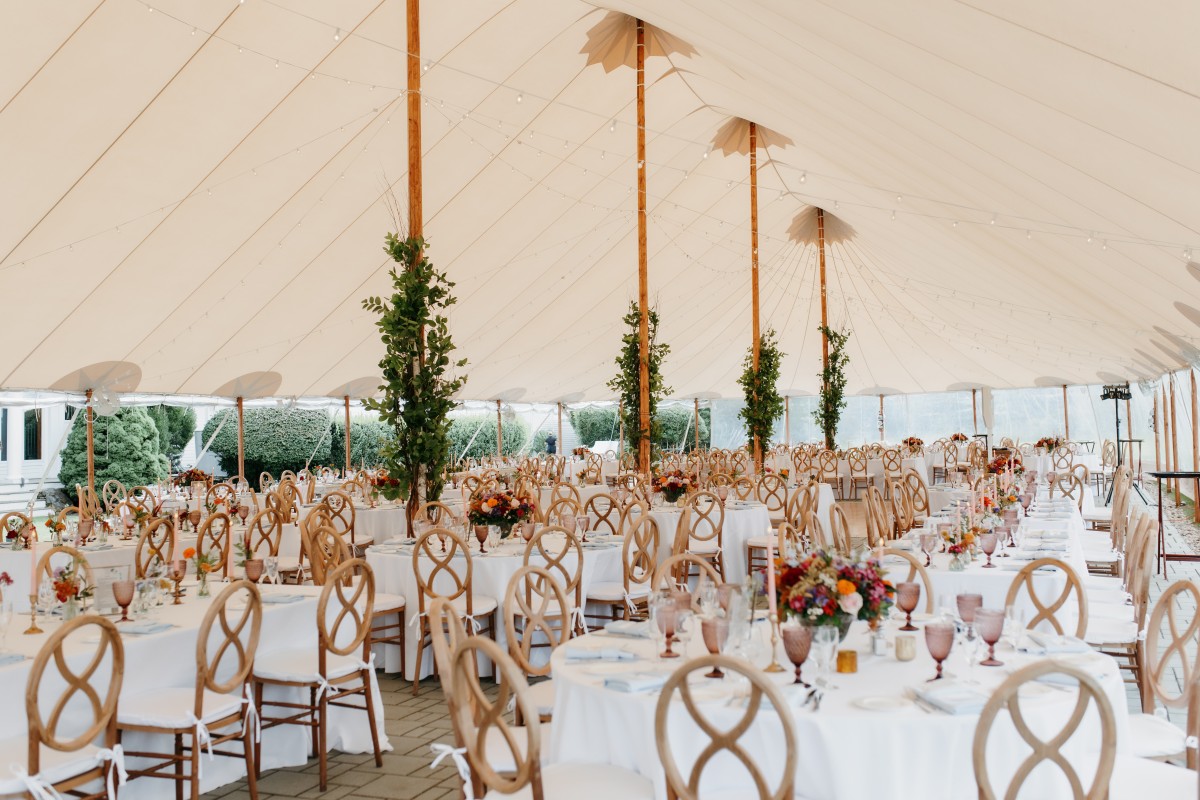 A beautifully decorated wedding tent featuring white linens and gold accents, exuding luxury and elegance.